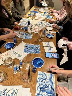 people sitting at a long table with paper and watercolors on it, making art