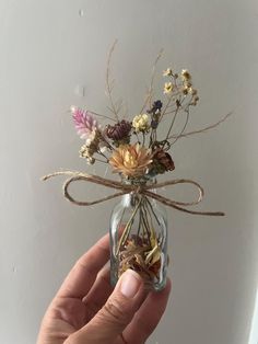 a hand holding a glass jar with dried flowers in it and a ribbon tied around the top