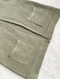 a close up of a knitted blanket on top of a white bed coverlet