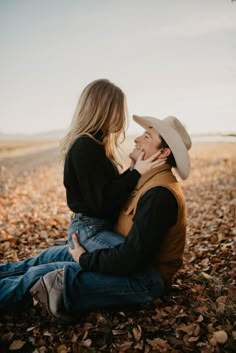 a man and woman sitting on the ground with leaves in front of them, looking into each other's eyes