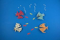 four different colored paper fish on a blue background