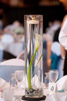 a tall vase with a flower in it on top of a white table cloth covered table