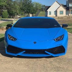 a bright blue sports car parked in front of a house on a driveway with grass and trees