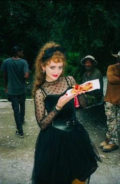 a woman in a black dress is holding a piece of paper with food on it