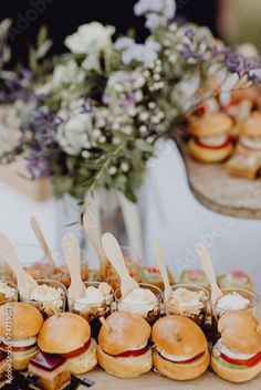 small sandwiches are arranged on trays with wooden spoons in front of them, along with flowers