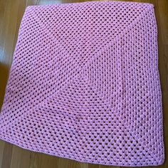 a pink crocheted blanket sitting on top of a wooden floor