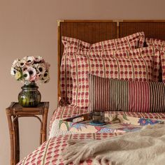 a bed with red and white checkered bedspread next to a table with flowers