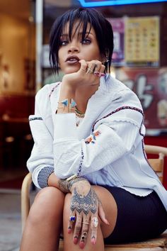 a woman sitting in a chair with her hand on her chin and tattoos on her arm