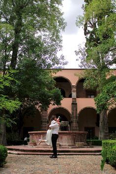 a man and woman standing in front of a building with trees on the other side