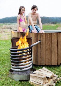 two people are sitting in an outdoor hot tub with fire and logs on the ground