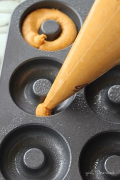 an orange doughnut being dunked into a muffin tin