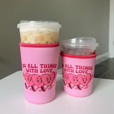 two pink cups sitting on top of a white table next to each other with lids