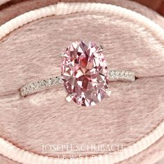 a pink diamond ring sitting on top of a cushion