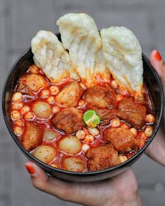 a person holding a bowl of food with meatballs and vegetables in sauce on it