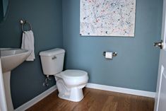 a white toilet sitting next to a sink in a bathroom under a painting on the wall