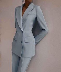 a woman in a light blue suit leaning against a wall with her hands on her hips