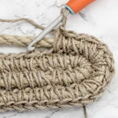 an orange handled crochet hook on top of a piece of jute