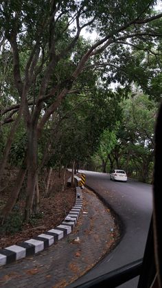 a car driving down the road next to some trees and bushes in front of it