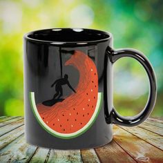 a black coffee mug with a watermelon print on it and a surfer riding a wave