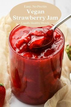 a strawberry jam in a glass jar with a spoon and strawberries on the side