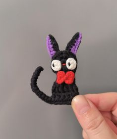 a crocheted black cat with a red bow tie is shown in front of a gray background