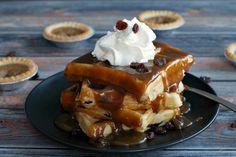 a stack of waffles topped with whipped cream and raisins on a black plate