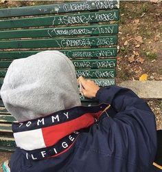 a person sitting on a bench writing on the back of his jacket and hood over their head