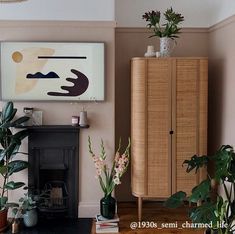 a living room filled with lots of plants next to a fire place and a painting on the wall