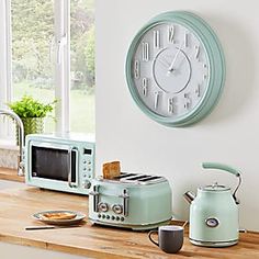 a clock mounted on the wall above a toaster and coffee pot sitting on a kitchen counter