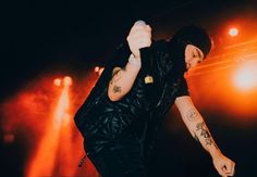 a man with tattoos on his arm holding a microphone in front of some bright lights