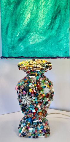 a lamp that is made out of beads and other items on a table next to a painting