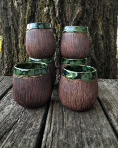 three vases sitting on top of a wooden table next to a tree in the woods