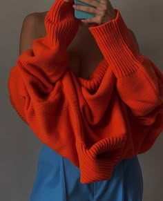 a woman wearing an orange sweater and blue skirt holding a cell phone in her hand