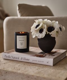 a candle and some flowers are sitting on a table next to a book that says pacific natural at home