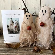 two cloth ghost dolls are next to a card and some autumn leaves on the ground