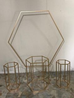 three gold geometric sculptures sitting on top of a stone floor