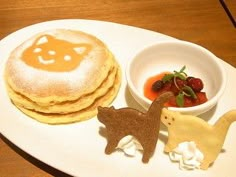 a white plate topped with pancakes covered in toppings next to a bowl of fruit