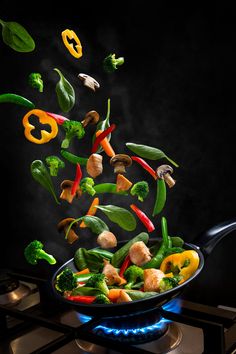 vegetables being tossed into a skillet on the stove top with steam rising from it