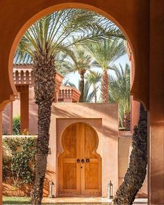 an archway leading to a building with palm trees in the foreground and grass on the ground