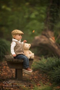 a little boy sitting on top of a bench with a teddy bear in his hand