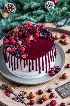 a red velvet cake with berries and nuts on a platter surrounded by pine cones