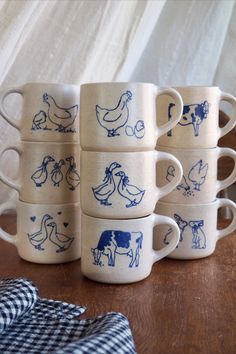 six coffee mugs with blue farm animals on them sitting on a table next to a plaid napkin