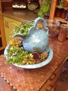 a blue teapot filled with green plants on top of a wooden table in a kitchen