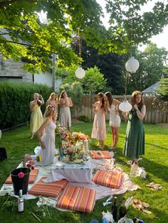 a group of women standing around a table with plates and drinks on it in the grass