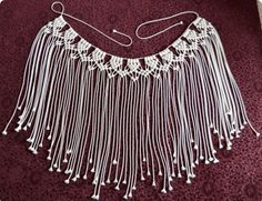 a white beaded necklace with fringes and beads on the bottom is laying on a purple surface