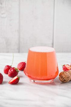 a glass filled with liquid next to strawberries on a white tablecloth and corks