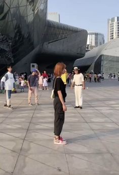 people are walking around in front of a building with a large sculpture on it's side