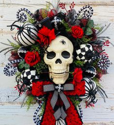 a skull wreath with red roses and black checkered ribbon on a white wooden wall