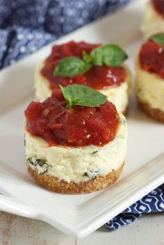 mini cheesecakes topped with fresh basil and sauce on a white square platter