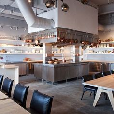 an industrial style kitchen with stainless steel appliances and tables in the foreground, surrounded by black leather chairs